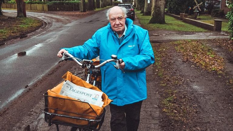 Alter Mann mit einem Fahrrad voller Zeitungen.